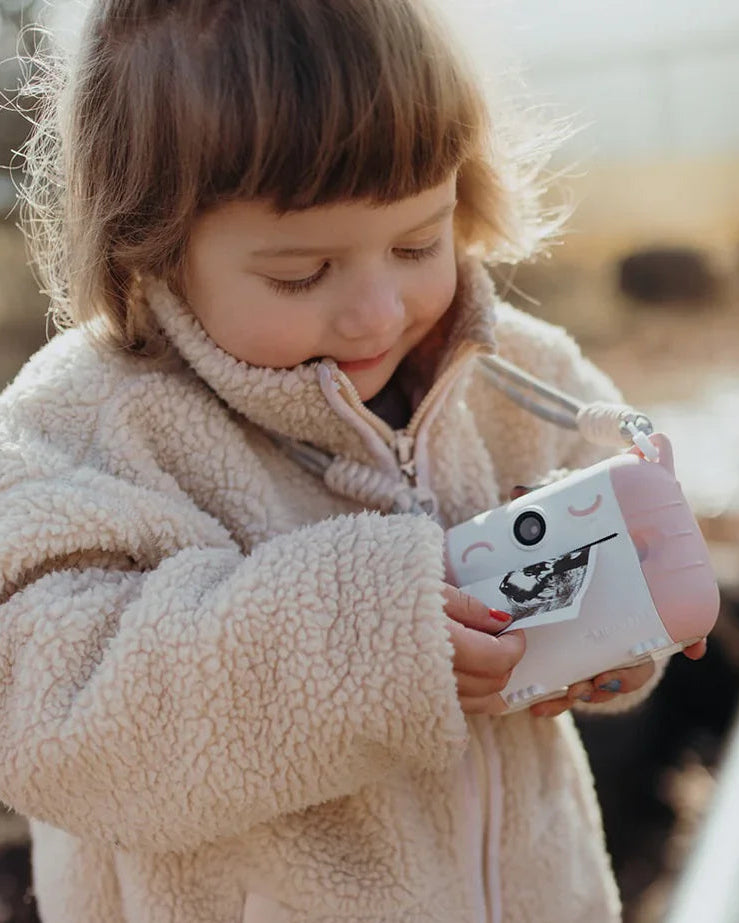 Child holding a pink kidywolf toy camera outdoors