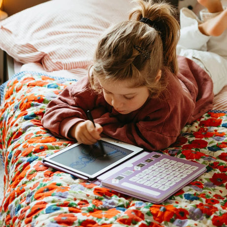 Child lying on a bed with a Kidywolf tablet and book, surrounded by colorful bedding.