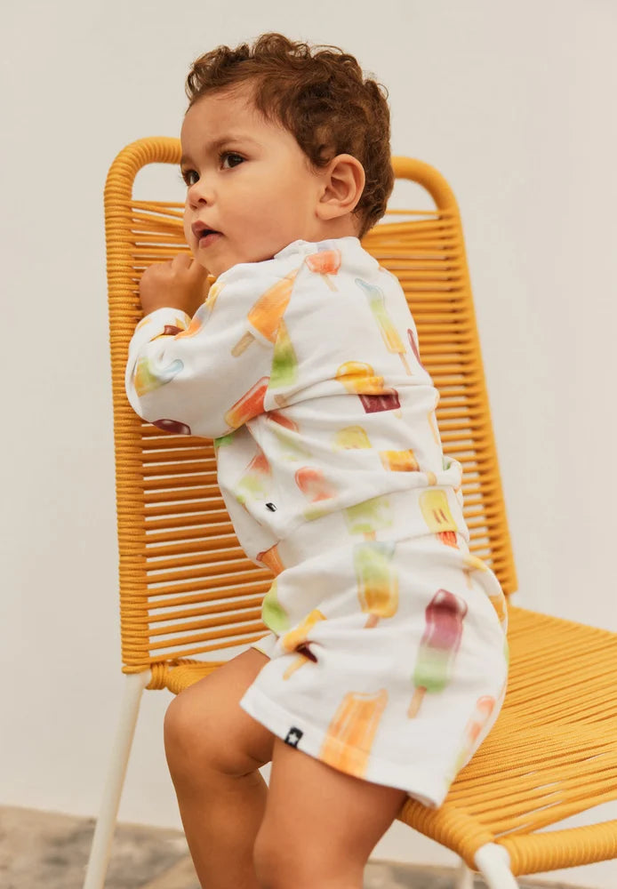 Child wearing a colorful ice cream set from Molo, sitting on a yellow chair against a neutral background