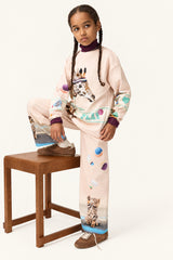 Young girl wearing a Molo pink set with animal prints sitting on a wooden stool against a white background