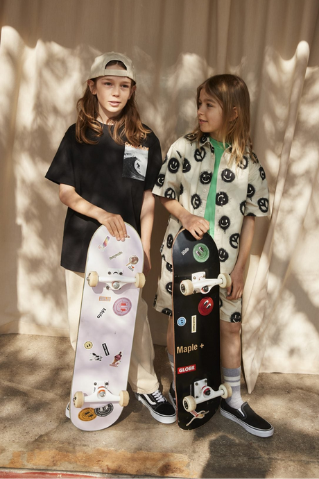 Two children wearing printed Molo t-shirts while holding skateboards against a neutral background