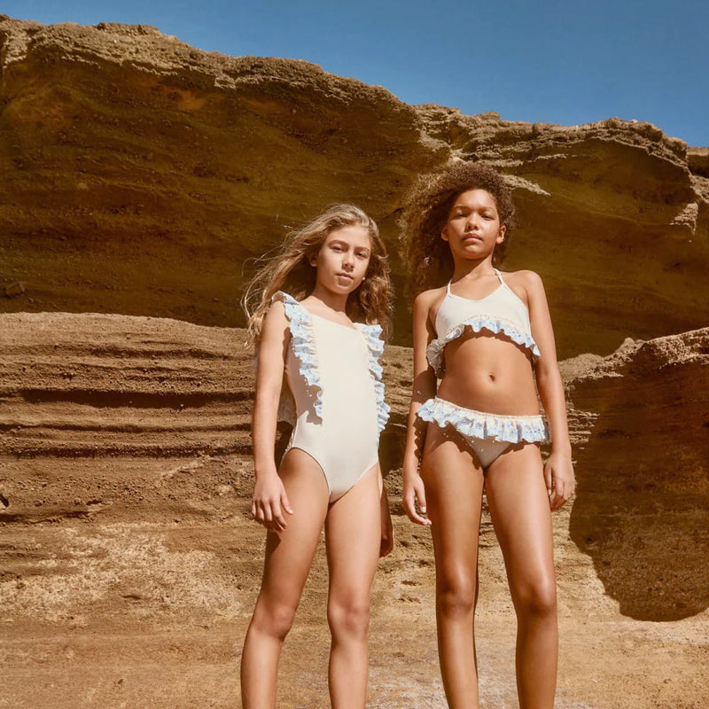 Two girls in Molo swimsuits standing against a rocky cliff.